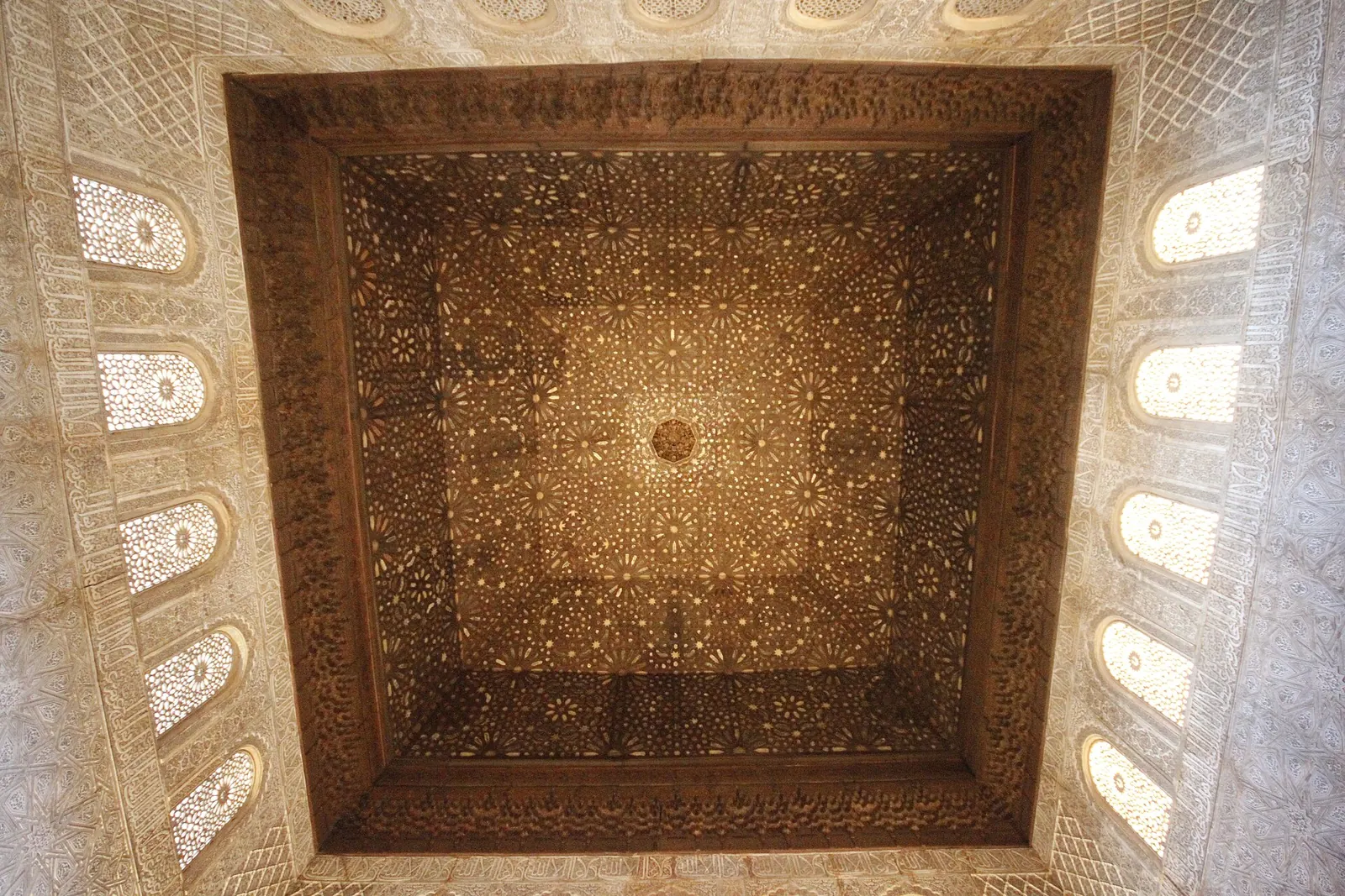 Un soffitto quadrato in legno intagliato con motivi a stella, circondato da finestre in stucco traforato, nella Sala degli Ambasciatori dell'Alhambra di Granada