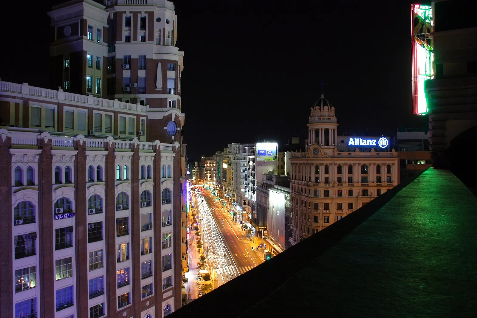 Veduta notturna lungo la Gran Vía di Madrid da un rooftop, con edifici illuminati e scie di fari delle auto lungo il viale